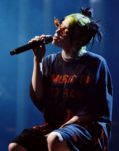 a woman with green hair and glasses on stage holding a microphone in her hand while she is