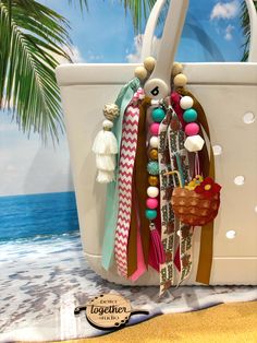 Elevate your beach or poolside style with the  Beach Bogg Bag Charm. This charming accessory adds a touch of summer flair to your favorite bag, making it perfect for sunny days by the water. The playful design of the charm embodies the carefree spirit of the season, while the vibrant colors capture the essence of summertime. With its whimsical appeal, this bag charm is sure to become a fun and eye-catching addition to your accessory collection. The tassel detail adds a trendy touch, ensuring that you stand out with a unique and stylish statement wherever you go. Bring a bit of beachside relaxation and poolside vibes to your look with this must-have summer bag charm. All of our key chains and/or charms make a perfect accessory to any bag.  They can be used on Bogg bags, sports bags, backpac Bohemian Bucket Beach Bag For Beach Season, Bucket Beach Bag For Beach Season, Bohemian Beach Bag Bucket Shape, Multicolor Beachy Beach Bag, Coastal Style Beach Bag For Vacation, White Coastal Style Bags For Beach, Multicolor Beach Bag With Tassels, Handmade Beach Bag For Vacation, White Beach Bag With Tassels For Summer