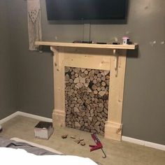 a tv mounted on the wall above a fire place with logs in front of it