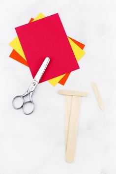 a pair of scissors and some construction paper on a white table with wooden pegs