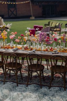 a long table with chairs and vases filled with flowers on it in front of a grassy area