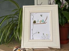 there is a picture frame with birds on the tree branch and shells in front of it