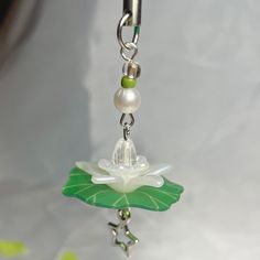 a green and white flower is hanging from a silver plated keychain on a chain