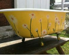 a yellow bath tub with daisies painted on the side sitting on a wooden bench