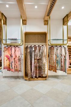 clothes are hanging on racks in a clothing store with tiled flooring and wooden beams