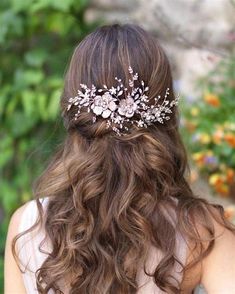 a woman with long brown hair wearing a white flowered headpiece in front of flowers