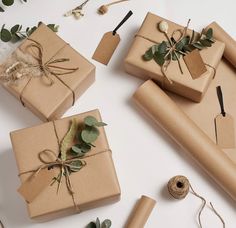 three wrapped presents with greenery and twine tied to them on a white surface