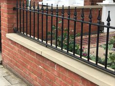 a black iron fence on the side of a brick building with flowers growing out of it