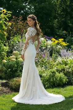 a woman in a wedding dress standing on the grass with her back to the camera