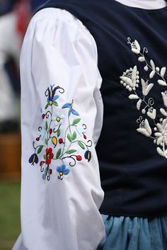 the back of a woman's blouse with embroidered flowers on it and blue pants