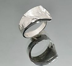 "Sea of Storms series was designed by the renowned Finnish goldsmith and jewelry artist Matti Hyvärinen in the 1960's inspired by the first lunar landings. Sea of Storms - Mare Procellarum is the biggest lunar \"sea\". This ring was made in 1974 in Matti's workshop in Turku, Finland. It is from our old stock - vintage, but never used. The size is adjustable so it fits most sizes. Material: 925 Sterling silver Measurements: width 12 mm on the front, 4 mm on the back Hallmarked: MJH, 925, Turku ci Modern Hand Forged Rings As A Gift, Modern Hand Forged Rings As Gift, Hand Forged Modern Rings As Gifts, Contemporary Polished Jewelry For Anniversary, Hand Cast Modernist Jewelry For Gifts, Modernist Hand Cast Jewelry As Gift, Modernist Hand-cast Jewelry For Gifts, Handmade Modern White Gold Rings, Modern Handmade White Gold Rings