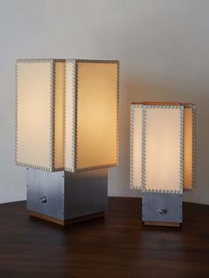 two lamps sitting on top of a wooden table next to each other, one is white and the other is silver