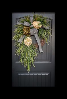 a wreath with pine cones and flowers hanging on the front door's black frame