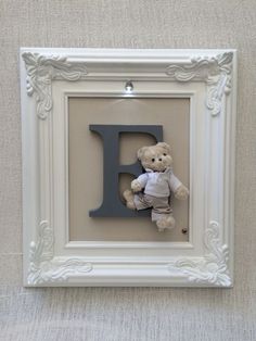 a teddy bear in a frame with the letter f on it's wall hanging