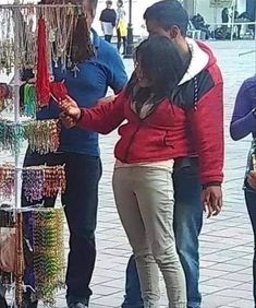 people are looking at jewelry on display in front of a store window, and one woman is trying to buy them