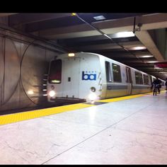 a subway train pulling into the station with people walking on the platform next to it