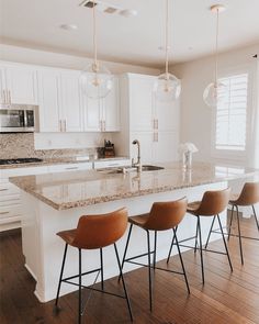 a kitchen with white cabinets and marble counter tops, four bar stools in front of the island