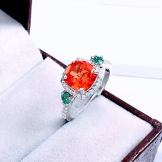 a ring with an orange stone surrounded by green and white stones