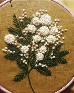 a close up of a embroidery on a piece of cloth with white flowers and green leaves