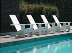 four white lawn chairs sitting next to a swimming pool