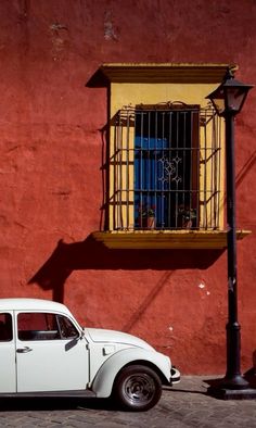 an old white car parked in front of a red building with a yellow window on the side