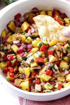 a hand dipping a tortilla chip into a bowl filled with pineapple salsa