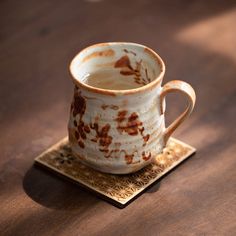 a brown and white coffee cup sitting on top of a wooden table next to a coaster