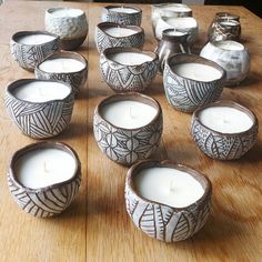 a table topped with lots of white candles sitting on top of a wooden table next to vases