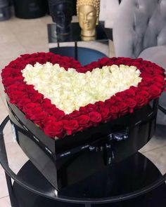 a heart shaped box filled with roses on top of a black table next to a gold statue