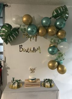 a birthday cake on a table with balloons and greenery in the shape of a wreath