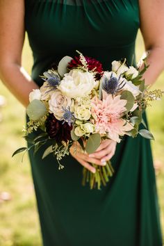 a woman in a green dress holding a bouquet with white and red flowers on it