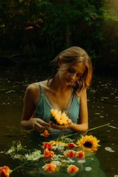 a woman in the water with flowers floating on her hands and looking down at her cell phone