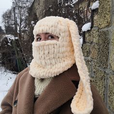 a woman wearing a knitted hat and scarf in front of a brick building with snow on the ground