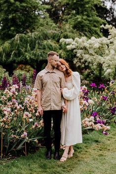 portrait of a couple standing together in front of a field of Iris's Photo Idea In Garden, Engagement Photos White Dress Field, Couple Floral Photoshoot, Engagement Garden Photoshoot, Vintage Garden Engagement Shoot, Garden Photo Shoot Couple, Photo Ideas In Garden, Farm Prenup Photo Ideas, Garden Couple Photoshoot Ideas