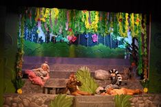 three people sitting on stone benches in front of a stage with plants and flowers hanging from the ceiling