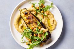 a white plate topped with an eggplant, chickpeas and hummus