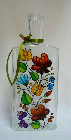 a glass bottle with flowers painted on the side and a green ribbon tied around it