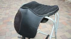 a close up of a black saddle on a metal stand with bricks in the background