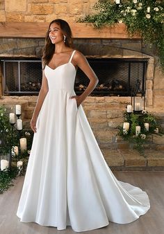 a woman standing in front of a fireplace wearing a white wedding dress with spaghetti straps