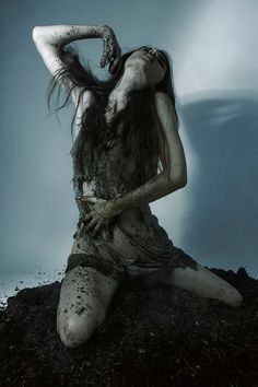 a woman covered in mud sitting on top of a pile of dirt with her hands behind her head