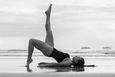 a woman in a black and white photo doing yoga on the beach with her legs up