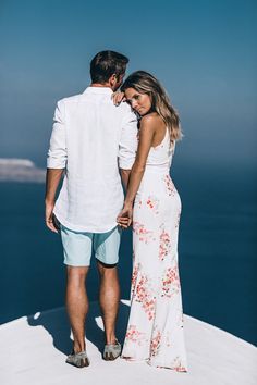 a man and woman standing on top of a snow covered hill next to the ocean