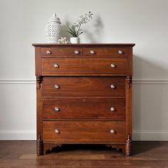 a wooden dresser sitting on top of a hard wood floor next to a white vase