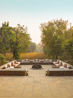 an outdoor seating area with benches and fire pit surrounded by trees in the middle of a field