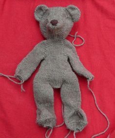 a gray knitted teddy bear laying on top of a red sheet