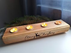 three candles are lit in front of a wooden plaque with merry christmas written on it