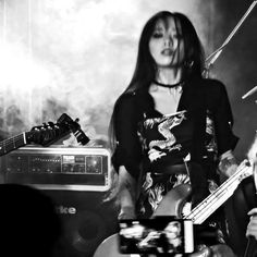 a woman with long hair holding a guitar and singing into a microphone in front of other instruments