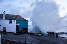 a large wave crashes into the side of a white building next to an ocean front