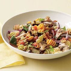 a white bowl filled with pasta salad on top of a yellow cloth next to a fork