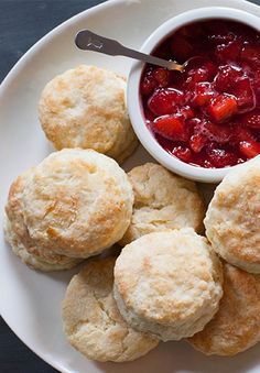 biscuits and jam on a white plate with a bowl of fruit in the middle,